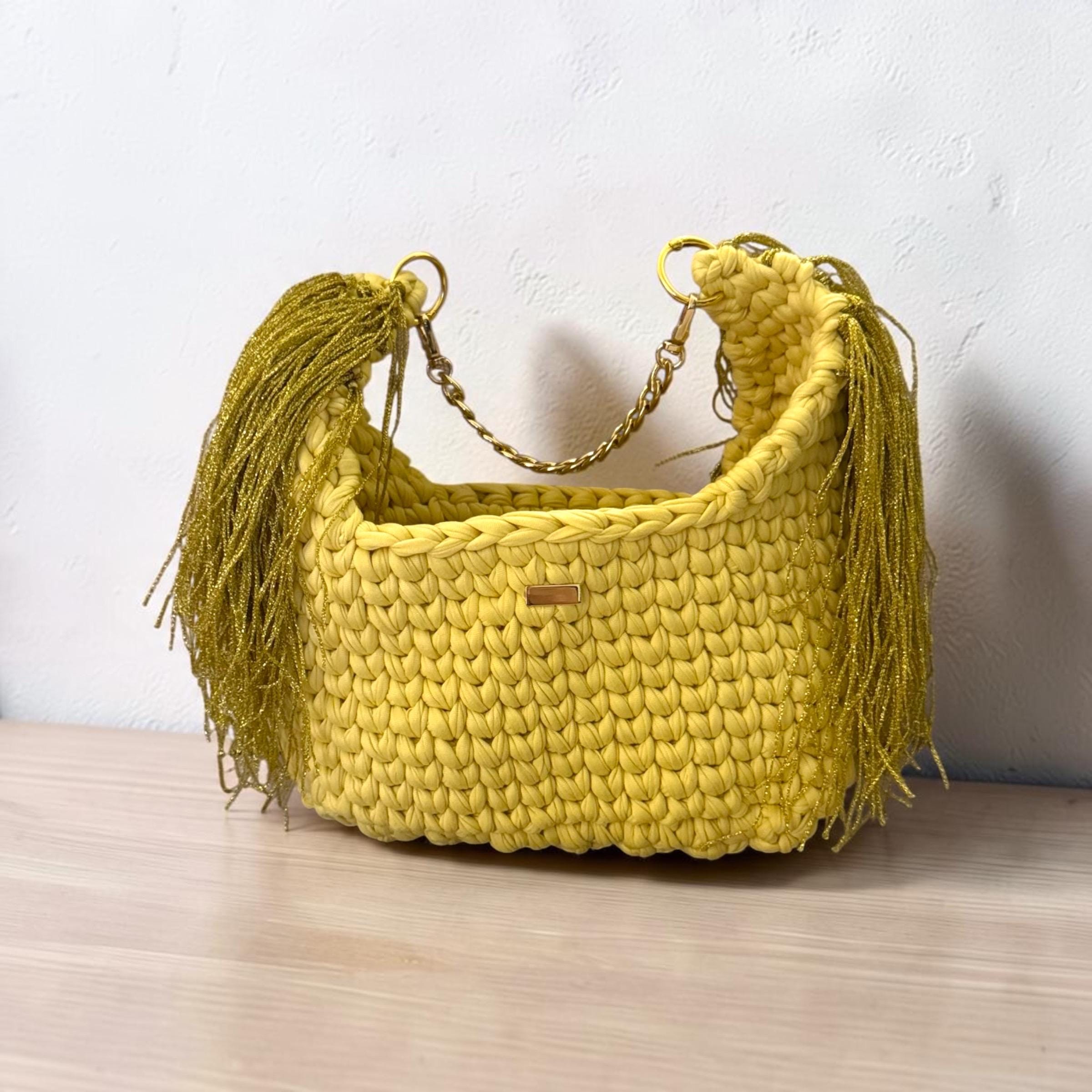 Light pastel yellow chunky crochet shoulder bag with gold tassels and a gold-tone chain strap