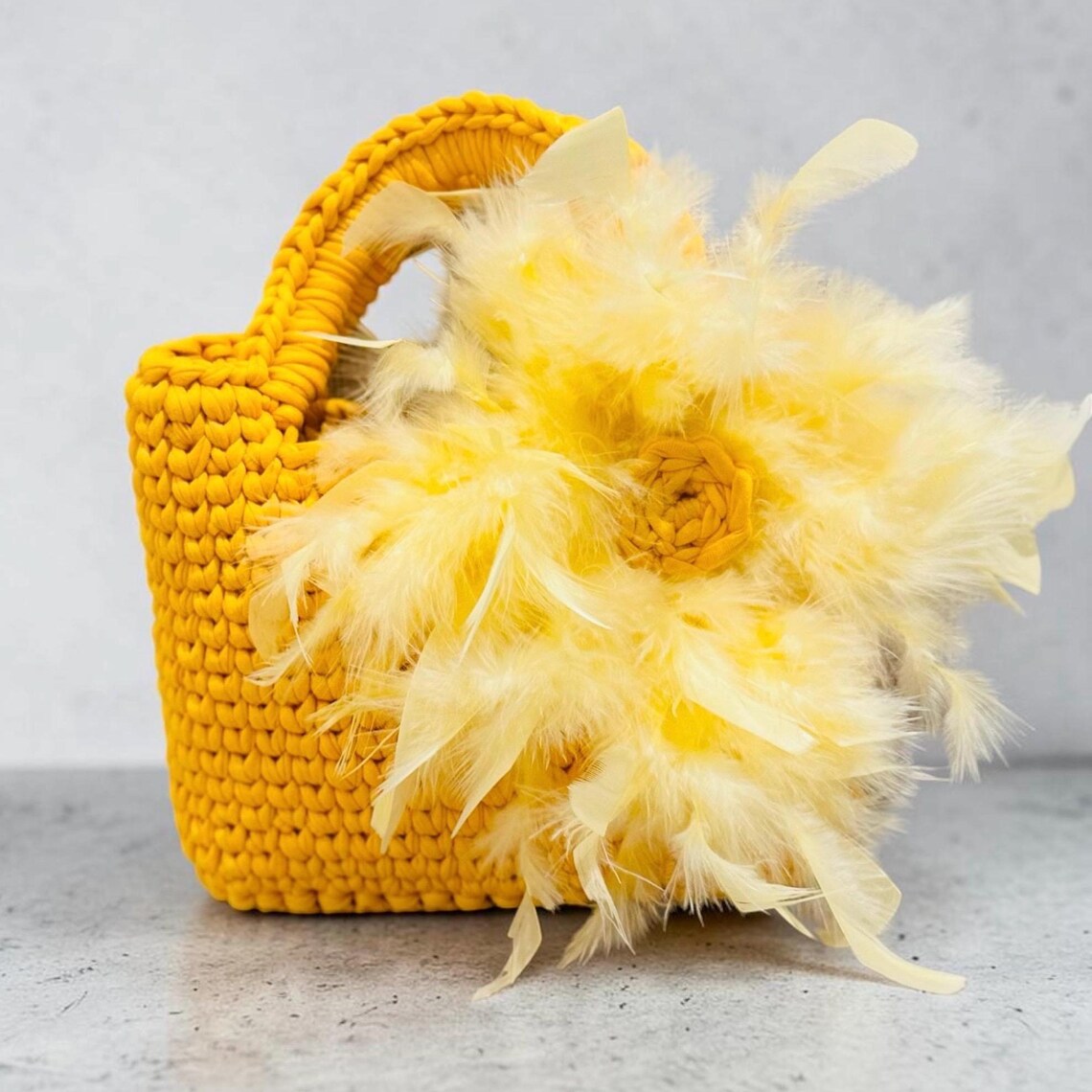 Yellow crochet purse with feather embellishments and faux leather bottom